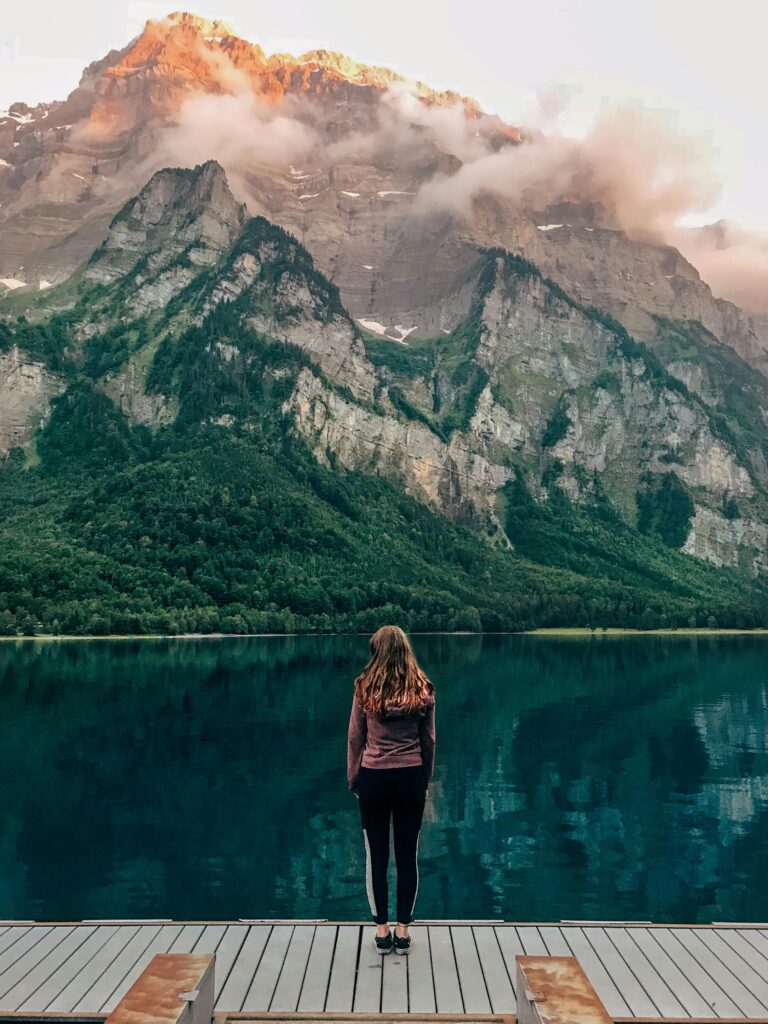 About Woman standing at Klöntalersee in Switzerland with scenic mountain background.